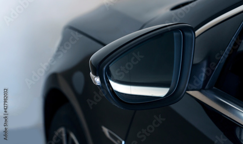 Close-up of the side left mirror and window of the car body black SUV on the street parking after washing and detailing in auto service industry. Road safety while driving.