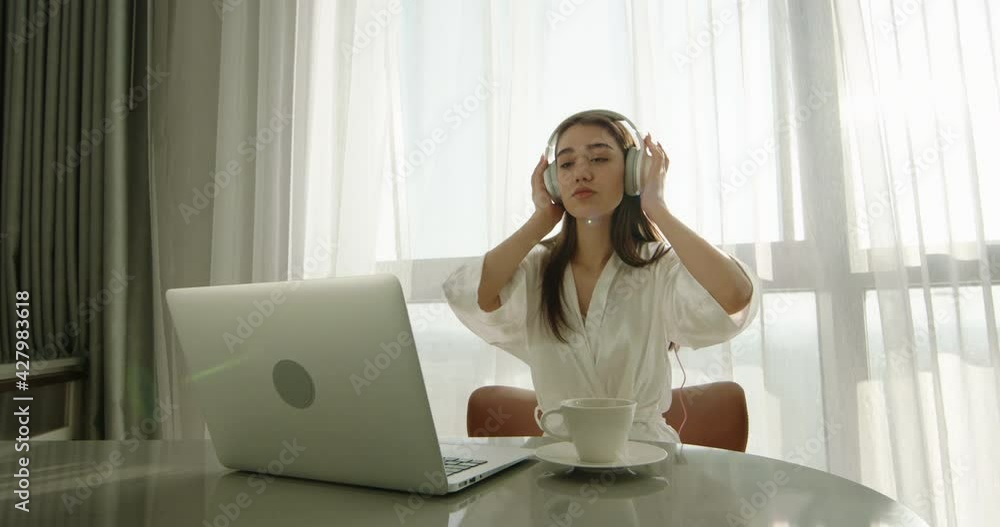 Joyful asian gen z girl wearing headphones and dancing in early morning. Positive teen having fun while using laptop computer 4k footage Joyful asian gen z girl wearing headphones and dancing in early morning. Positive teen having fun while using laptop computer 4k footage