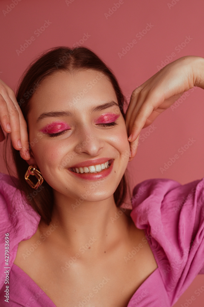 Happy smiling beautiful woman with pink, fuchsia color eyeshadow makeup, flawless clean skin, wearing elegant golden earrings, pink blouse. Spring, summer fashion trends
 - obrazy, fototapety, plakaty 