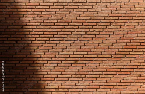 Red brick pattern. Old brick wall with cracks and scratches. Horizontal brick wall background with hard shadow. Vintage house facade.