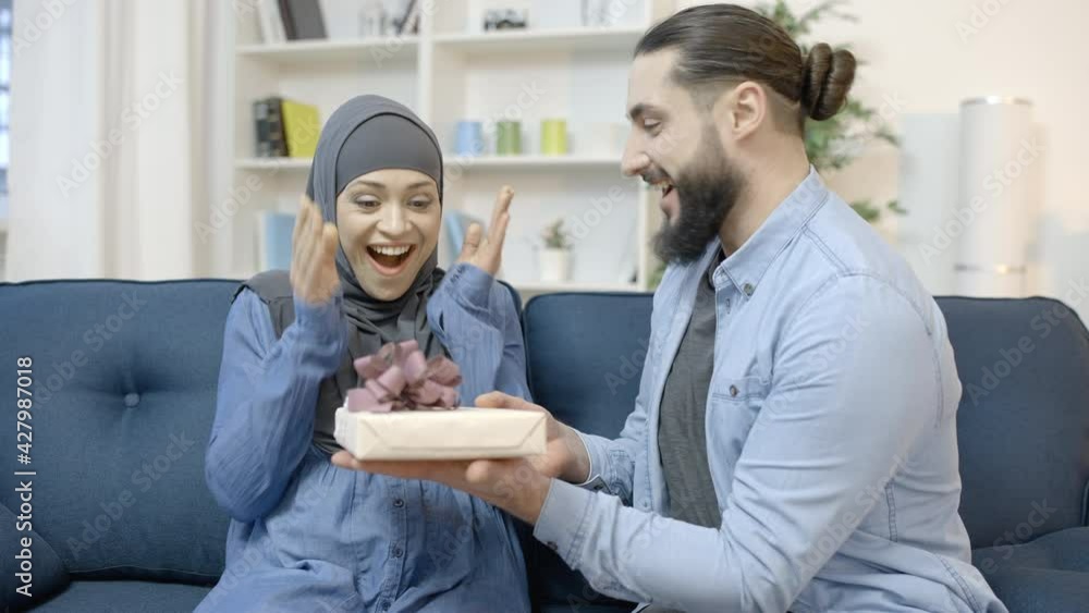 Arabic man presenting gift to surprised wife, excited woman hugging husband Arabic man presenting gift to surprised wife, excited woman hugging husband
