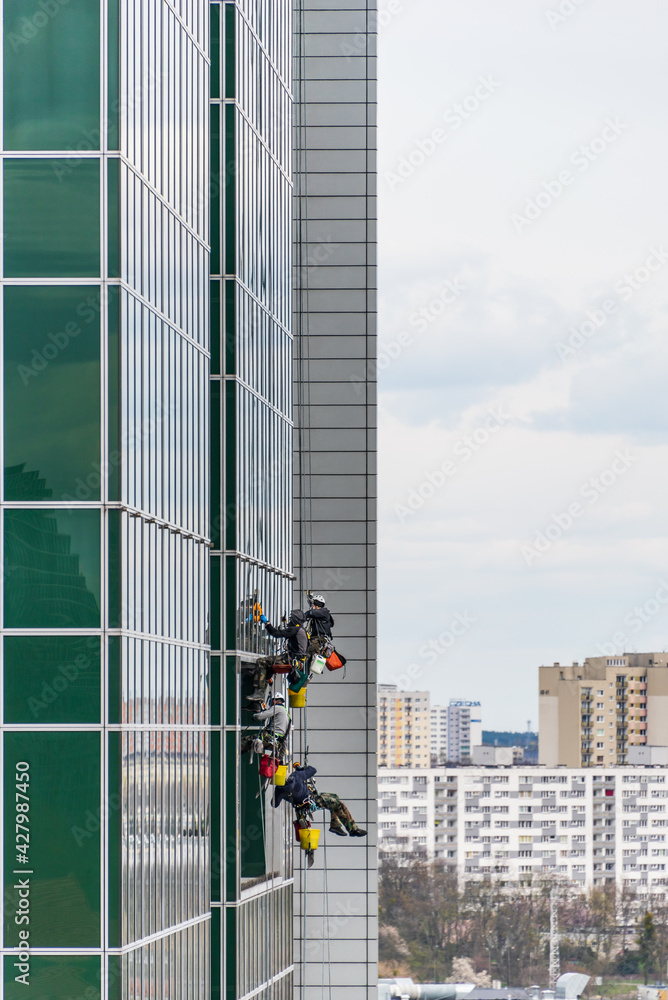 Workers cleaning windows and  the glass facade of a modern office building. The high rise window cleaning service workers use specialized equipment to access and clean windows of skyscraper.