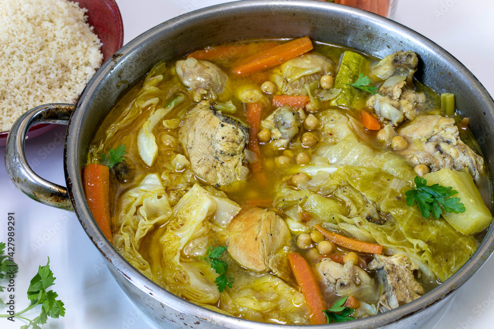 Stewed chicken with vegetables and hummus in a large iron saucepan.