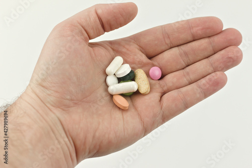 A handful of pills in a man's hand on a white background.