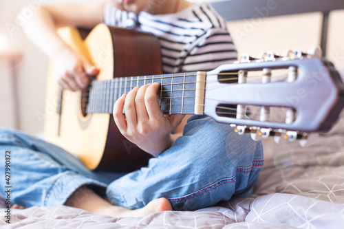 The child plays an acoustic guitar at home. Learning to play a musical instrument online, music school. Hands on guitar strings, close-up, selective focus. Lifestyle, positive emotions, inspiration.