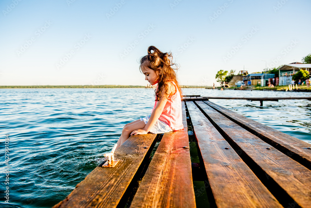 Cute little girl on the beach. The kid is resting by the sea. Summer vacation. Girl in the summer. A beautiful little girl sits on the pier by the water. girl lying on a wooden bench on the beach. 