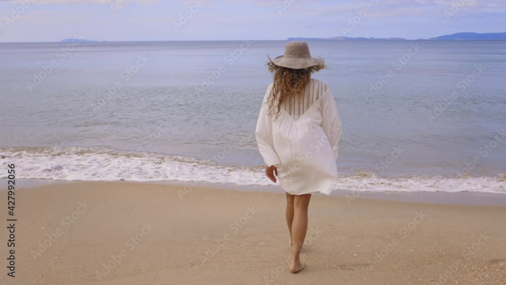 Woman in white dress walking along a tropical beach Woman in white dress walking along a tropical beach