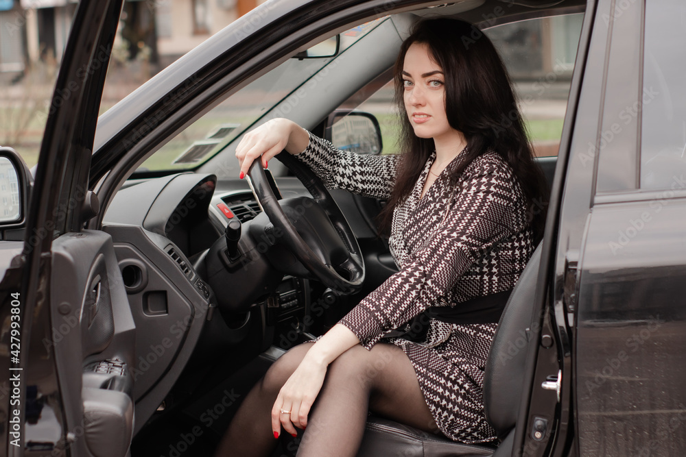 portrait of attractive brunette in grey checkered dress in a black car. girl in automobile. business woman