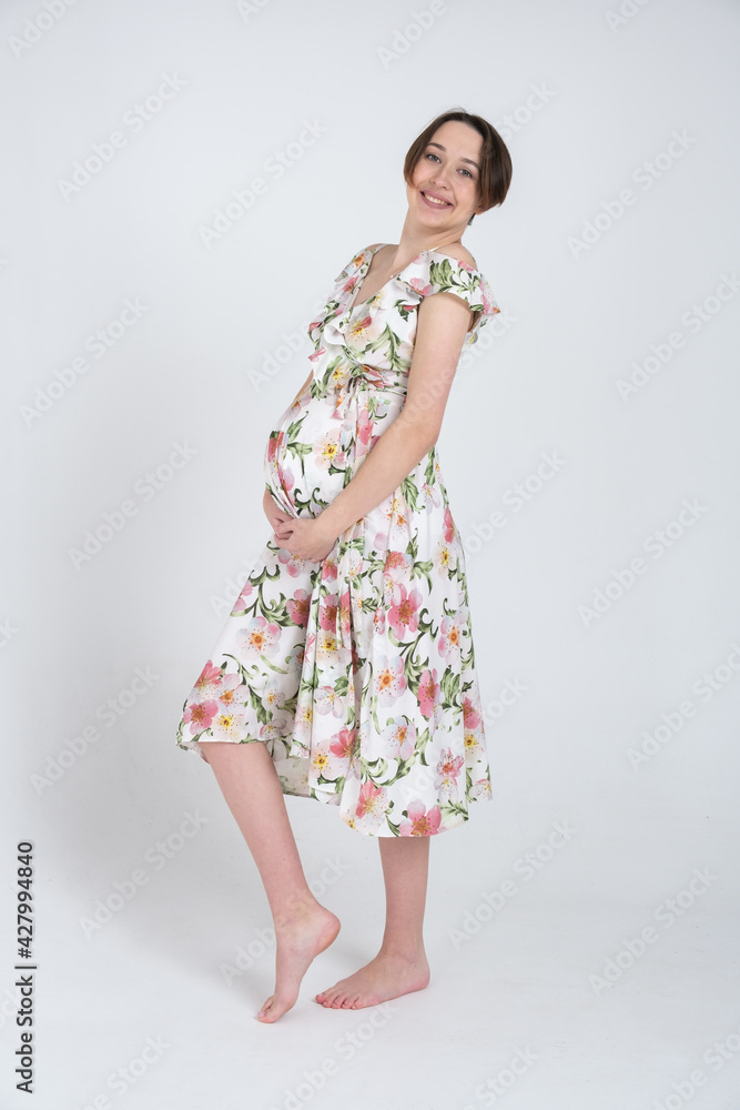 Studio portrait of cheerful young pregnant woman in summer dress on white gray background, happy pregnancy concept Studio portrait of cheerful young pregnant woman in summer dress on white gray background, happy pregnancy concept