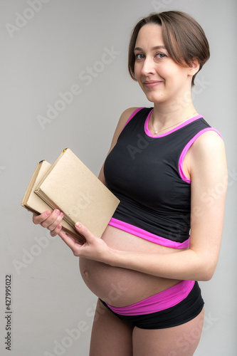 Studio portrait of young adult pregnant woman holding stack of books, preparing for babybirth concept, white background photo