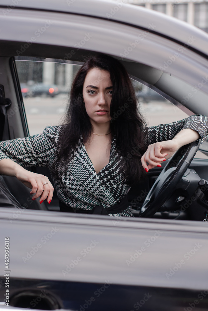 portrait of attractive brunette in grey checkered dress in a black car. girl in automobile. business woman