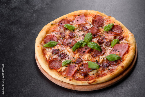 Delicious fresh oven pizza with tomatoes, salami and bacon on a dark concrete background