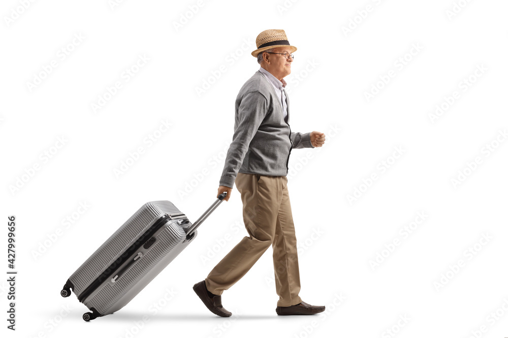 Full length profile shot of an elderly man walking and pulling a suitcase Full length profile shot of an elderly man walking and pulling a suitcase