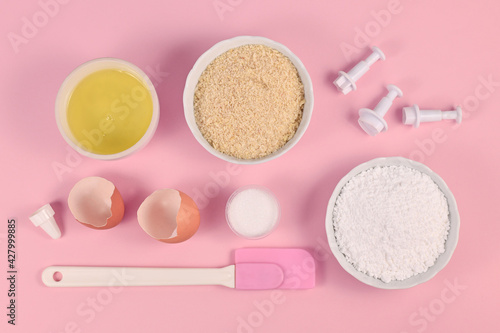 Ingredients for making homemade French Macarons sweets including powdered sugar, ground almonds, egg white, salt and baking tools on pink background