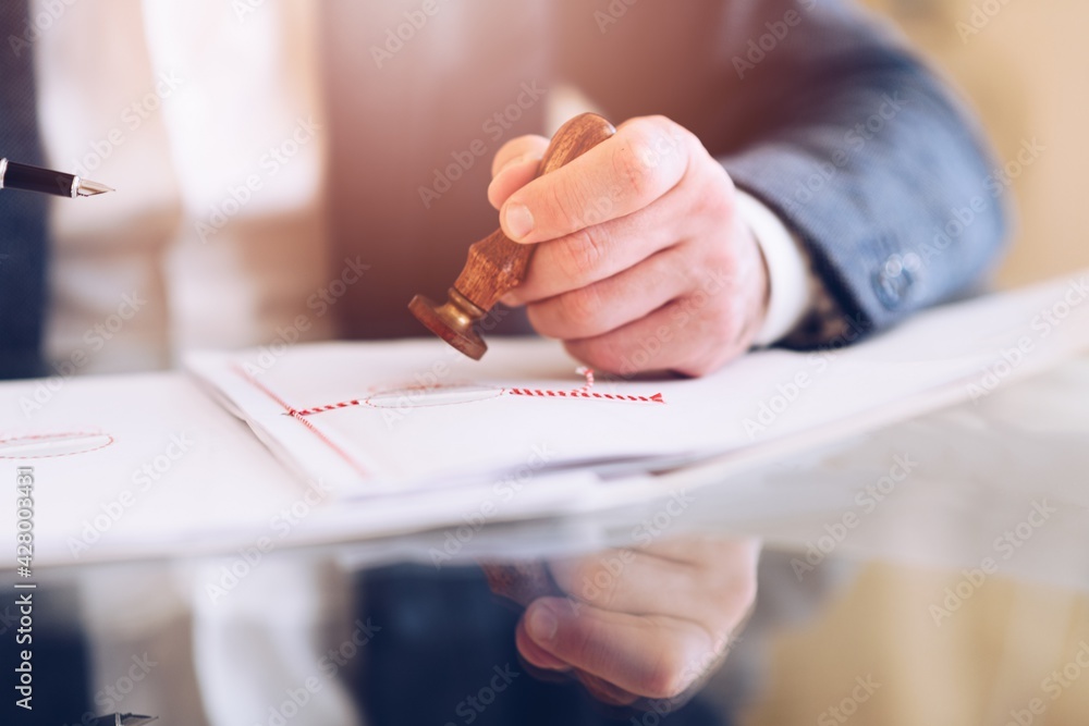 The lawyer's hand stamps a notary seal on the contract paper or a certificate in the office.