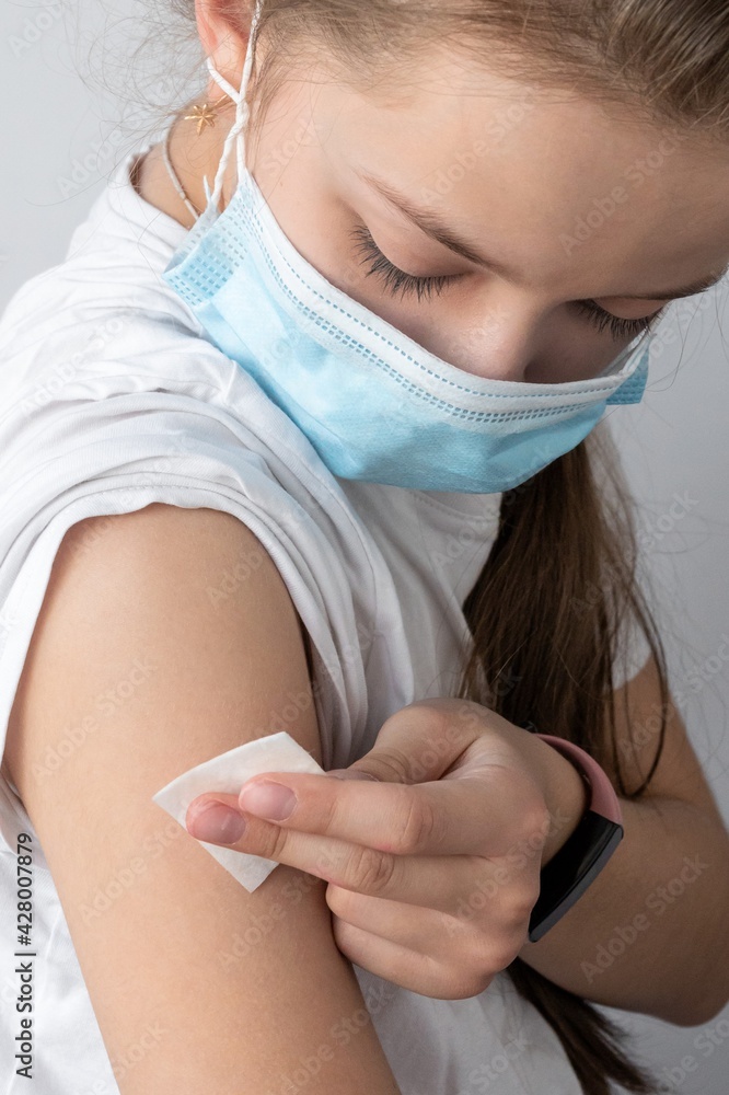 girl in a medical mask holds cotton wool on her hand after the injection. The concept of medicine and vaccination