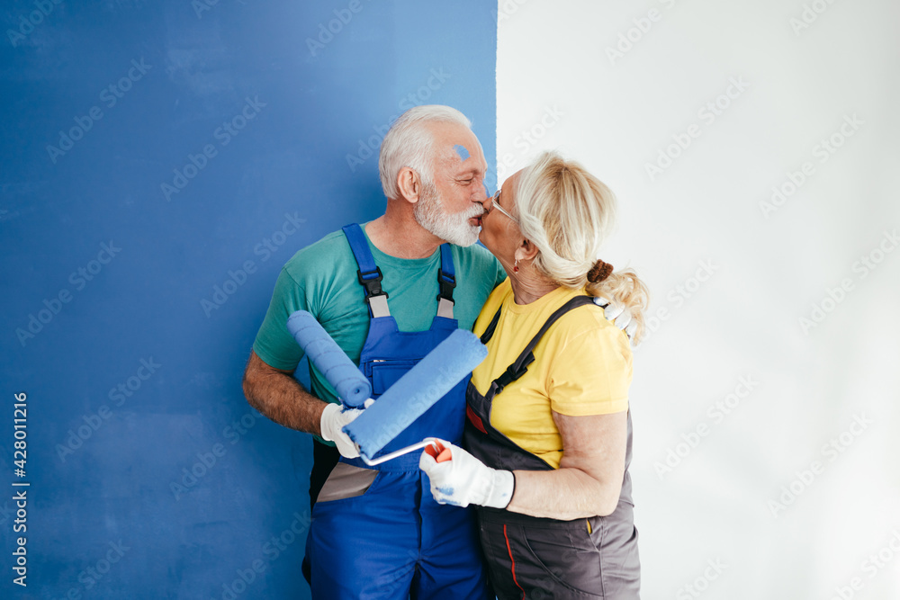 Happy senior couple renovating their home. They are painting a wall together. Happy senior couple renovating their home. They are painting a wall together.