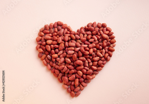 Peanuts are laid out in the shape of a heart on a pastel background. Flat layer . Top view