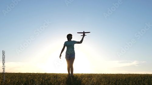 Child plays with a toy airplane. Slow motion. Girl wants to become pilot and astronaut. Happy girl runs with a toy airplane on field in the sunset light. Teenager dreams of flying and becoming pilot.