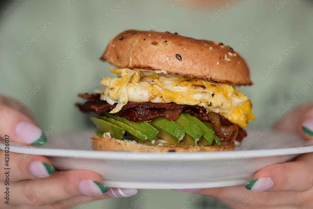 Closeup woman's hands holding a plate with breakfast bagel sandwich Closeup woman's hands holding a plate with breakfast bagel sandwich