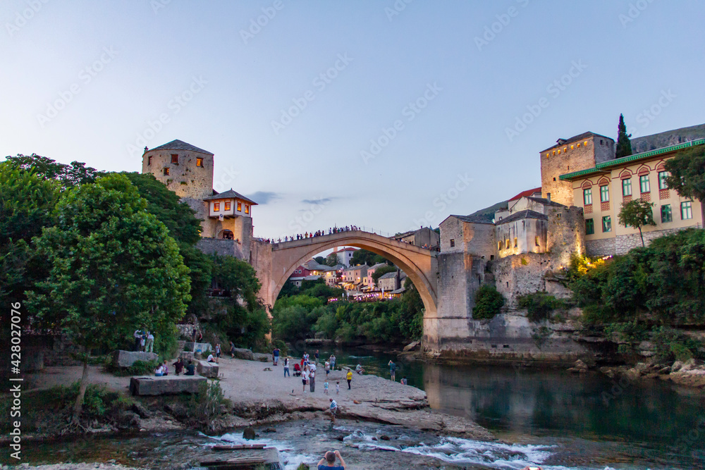 View on Old Bridge in Mostar, Bosnia-Herzegovina from the beach over the river in the sunset during sunny summer day.