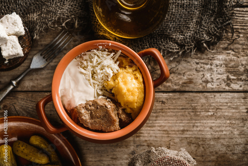 Delicious polenta with meat, cheese and sour cream in the bowl on rustic wooden background. Traditional romanian food, top view © Jukov studio