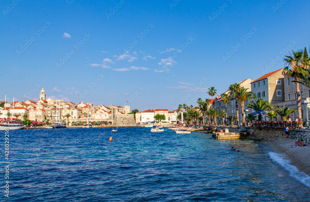 View of Korcula shore during sunny summer day, beautiful small city with red roofs buldings and cristal water.