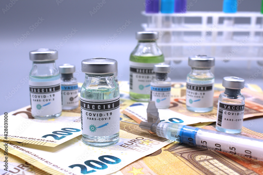 Vaccine vials next to a syringe and on euro banknotes