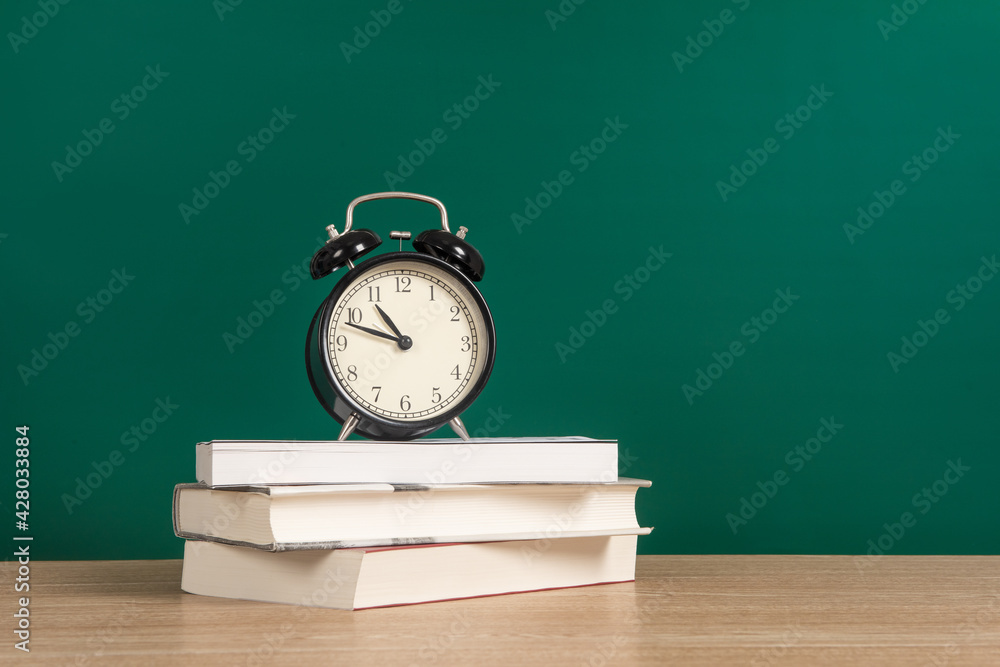 Alarm clock on stack of textbook with chalkboard background copy space Alarm clock on stack of textbook with chalkboard background copy space
