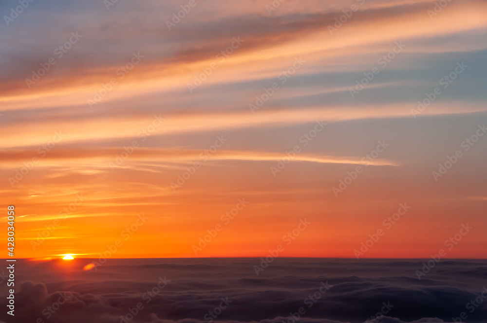 Magnificent scene above the clouds of the orange sunset with beautiful clouds in high relief coloring the sky. Amazing scene seen from an airplane. Feeling of floating.