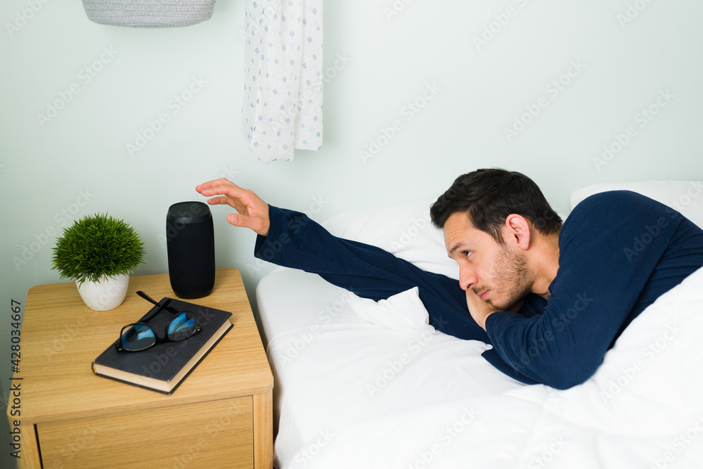 Obraz premium Tired man waking up by the sound of the alarm