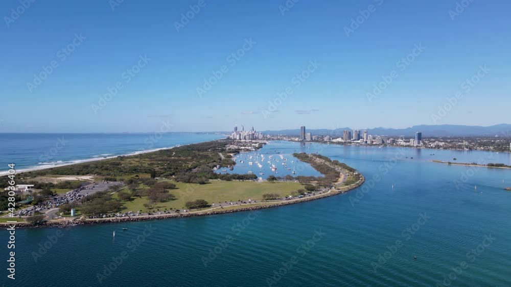 High static drone view of a man-made ocean inlet and safe boat harbor with a metropolitan skyline and mountain range in the distance. High static drone view of a man-made ocean inlet and safe boat harbor with a metropolitan skyline and mountain range in the distance.