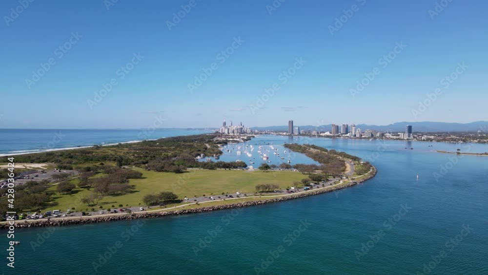 High revealing drone view of a man-made ocean inlet and safe boat harbor with a metropolitan skyline and mountain range in the distance. High revealing drone view of a man-made ocean inlet and safe boat harbor with a metropolitan skyline and mountain range in the distance.