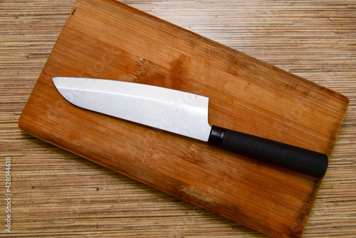 Cutting board and a kitchen knife on wooden background. Top view