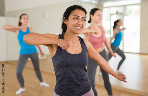Positive adult Latina enjoying active dances in female group in modern dance studio.