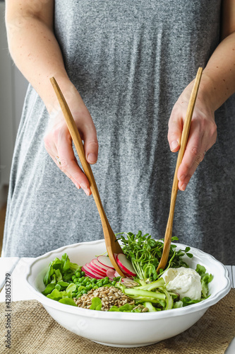 Female hands using wooden salad spoons to toss fresh spring salad