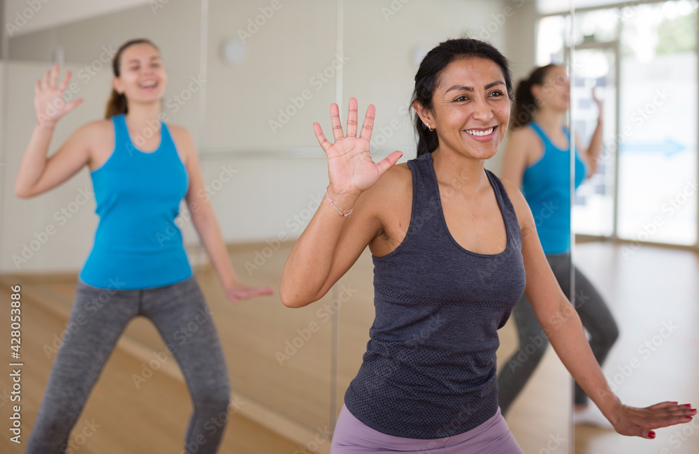 Cheerful hispanic woman practicing vigorous lindy hop movements in group dance class.