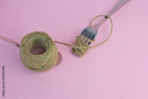 Fork and spoon with a twine rope on a pink background photo