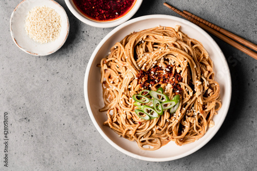 Spicy sesame noodles in a bowl next to chile oil and sesame seeds. photo