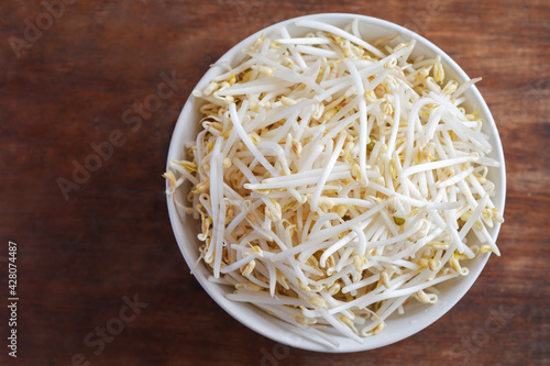 Bean sprouts in a white ceramic cup placed on a brown wooden table, the view from the top.