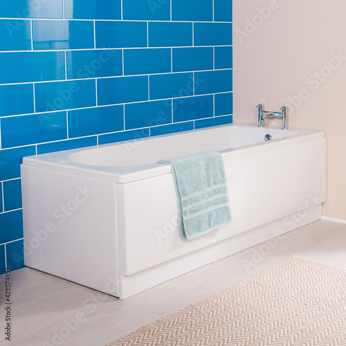 Angled side view of a sleek modern bathtub next to a blue brick wall in a bright room photo