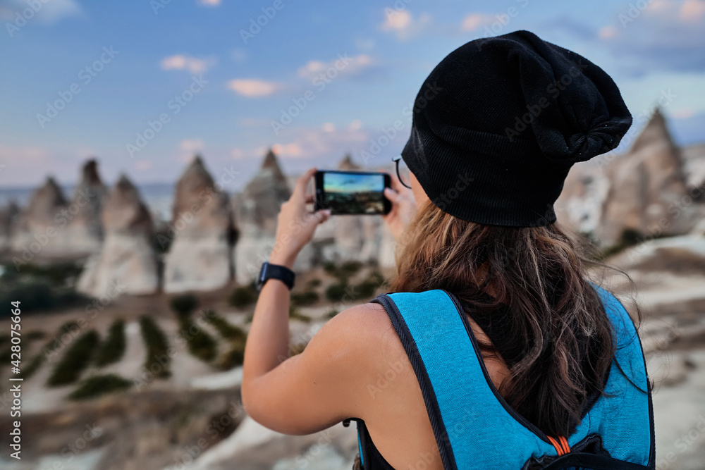 Beautiful tourist woman taking picture of Stone houses on her smartphone in Love valley in Goreme village.
