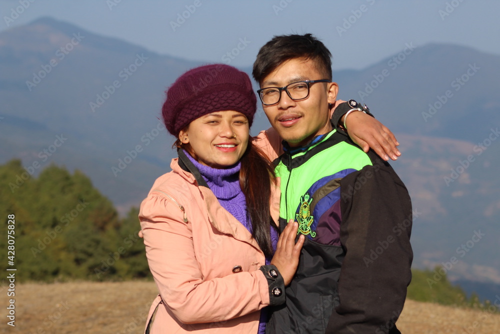 A Nepali couple is smiling and wearing jacket in front of jungle