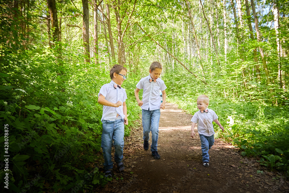 Boys in a white shirts and a pink butterfly in nature among the greenery. Funny walk of three brothers in the park or forest