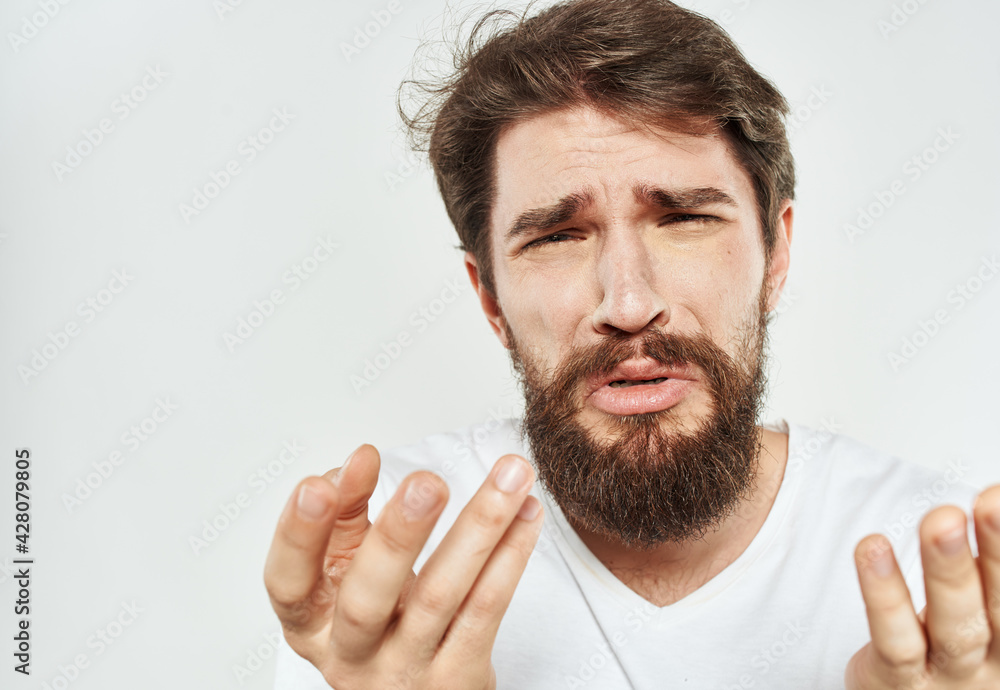 Fototapeta premium A man gestures with his hands on a light background in a white t-shirt cropped view