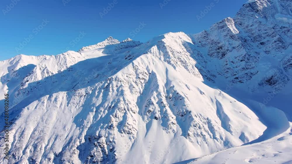 Picturesque high snowy mountains under clear blue sky at bright sunlight in Elbrus region on winter day aerial motion Picturesque high snowy mountains under clear blue sky at bright sunlight in Elbrus region on winter day aerial motion