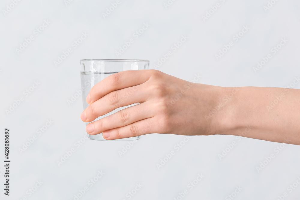 Female hand with glass of water on grey background Female hand with glass of water on grey background