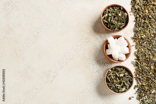 Bowls of dry green tea and sugar on light background