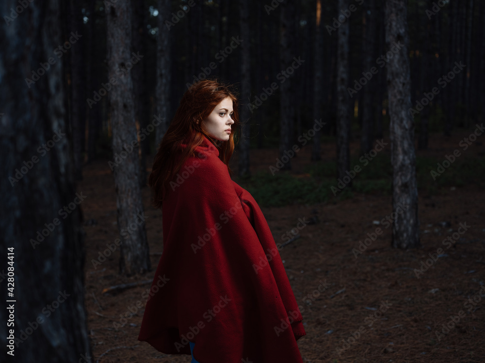 Beautiful woman with a red cape near the trees in the forest Beautiful woman with a red cape near the trees in the forest