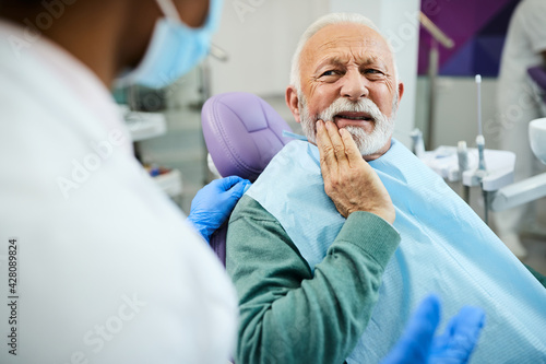 Senior man complaining about toothache to his dentist at dentist s office.